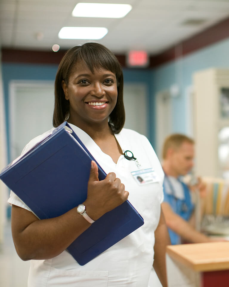 smiling nurse holding a binder in front of a medical reception desk
